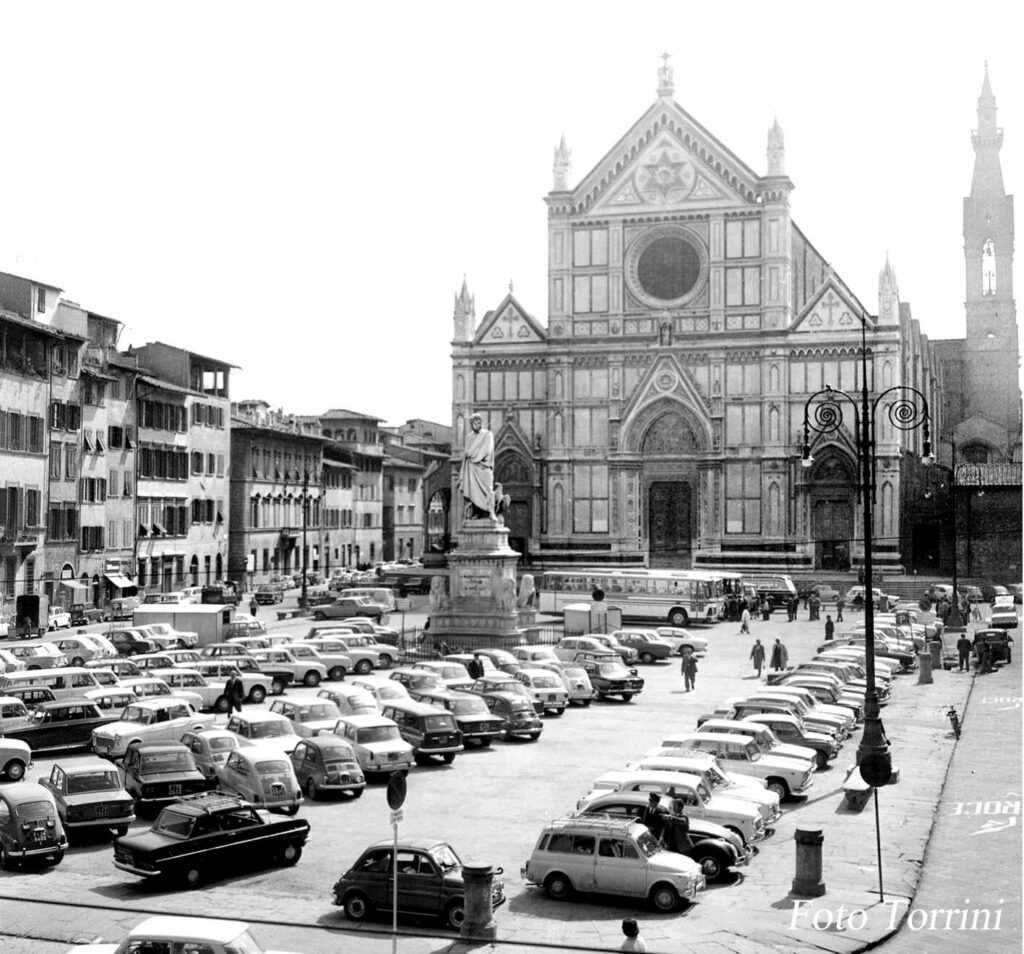 A black and white photo of cars parked in front of a church.